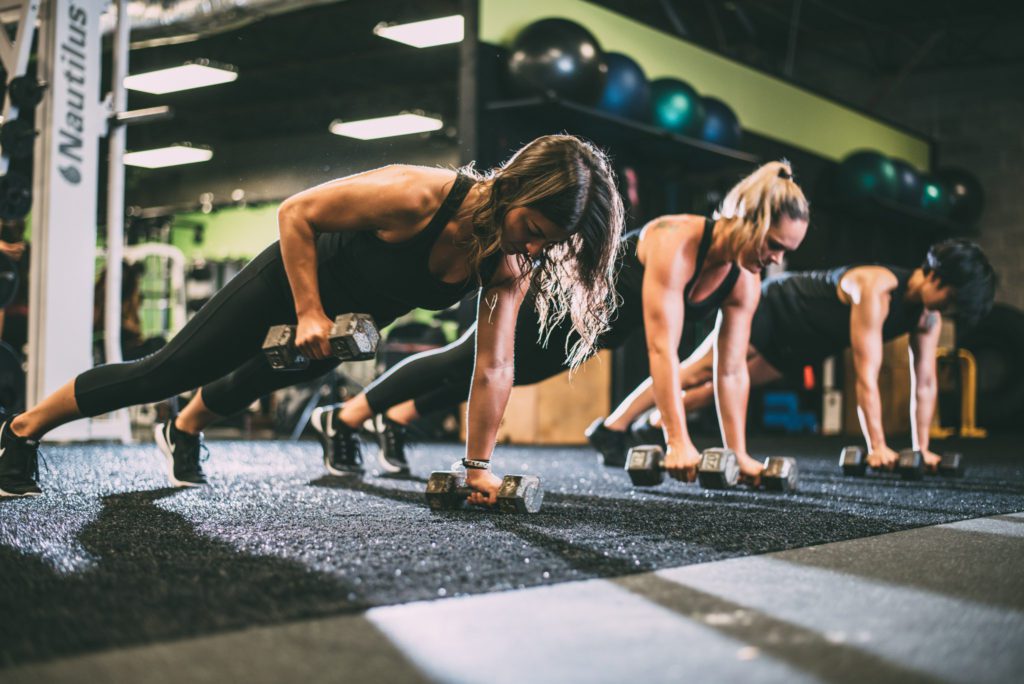 Group performing dumbbell plank rows in gym